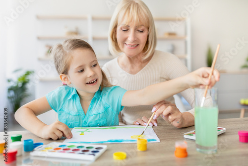 Photos Elderly babysitter teaching little girl drawing, helping improve creative abilities, develop artist talent