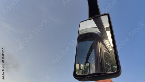 Side mirror of a truck reflecting the vehicle cabin against a clear blue sky.Truck rearview mirror with reflection detail, captured outdoors under a bright sky.