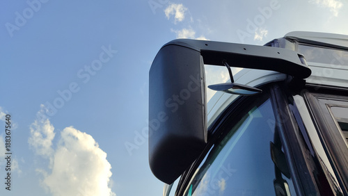 Side mirror of a truck reflecting the vehicle cabin against a clear blue sky.Truck rearview mirror with reflection detail, captured outdoors under a bright sky.
