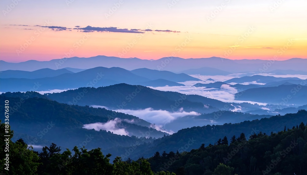Obraz premium A scenic panoramic view of layers of mountains during dawn or dusk, with wisps of fog in the valleys and a colorful sky
