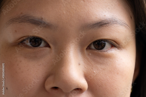 Asian woman facing camera, filling frame, showing skin texture and pupil reflection in studio light