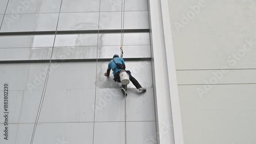 A window cleaner climbs a high-rise building using ropes and harness to ensure a spotless finish