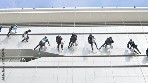 Professional window cleaners work efficiently on commercial building's facade, showcasing teamwork and safety in high-rise cleaning on a clear day, emphasizing modern industrial pr