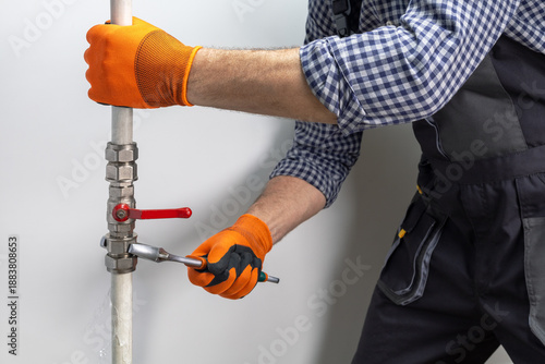 A plumber in uniform is working on a pipe that is dripping water. Fix water plumbing leaks in outdoor.