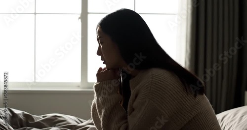 Woman sitting on bed looking sad.