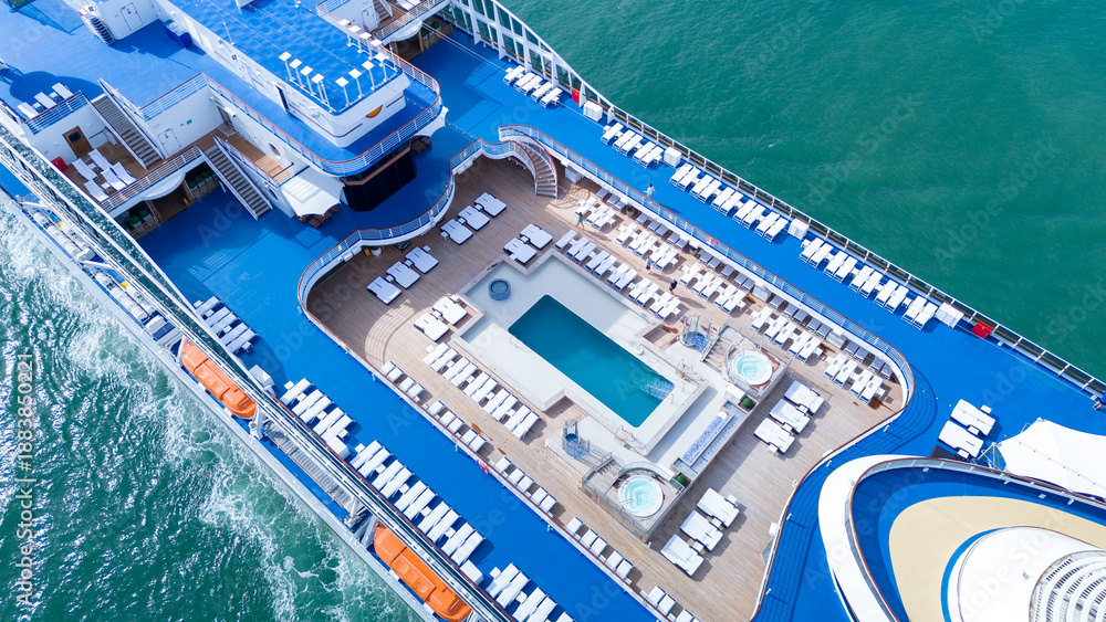 Fototapeta premium a luxury cruise ship's open deck featuring a swimming pool, jacuzzis, and rows of sunbeds. Multi-level recreational area with wooden flooring and blue decks over the ocean.
