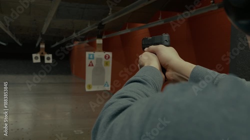 POV of person actively shooting handgun at paper targets inside an indoor shooting range. Controlled firearm use, marksmanship training, safe target practice.