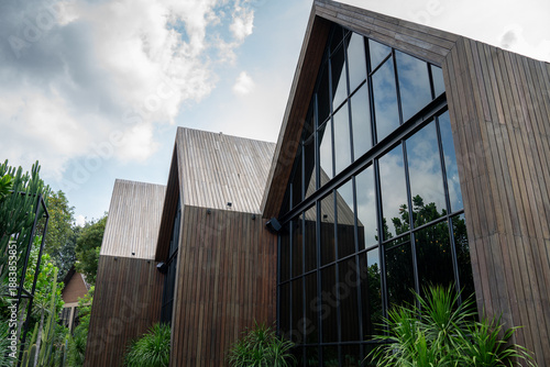Wallpaper Mural barn house architecture with wooden facade and large glass windows under a cloudy sky. This contemporary exterior design with tropical garden is ideal for real estate and luxury living Torontodigital.ca