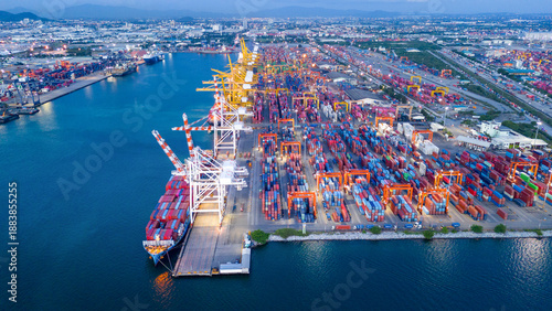 a busy deep-water cargo container port terminal during the twilight blue hour. Logistics center illuminated by industrial lights with gantry cranes and shipping vessels. Global trade infrastructure.