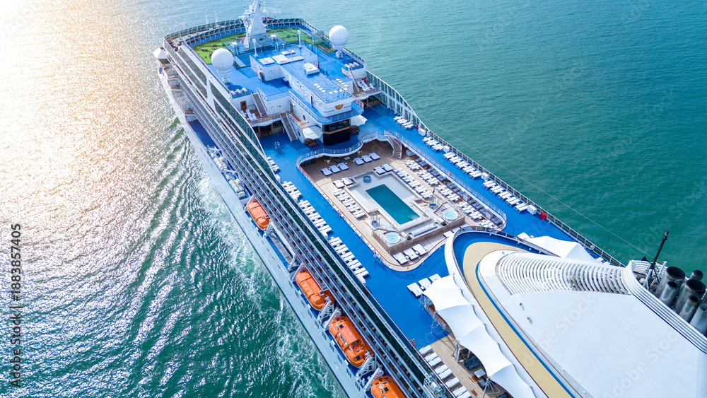 Naklejka premium a luxury cruise ship's open deck featuring a swimming pool, jacuzzis, and rows of sunbeds. Multi-level recreational area with wooden flooring and blue decks over the ocean.