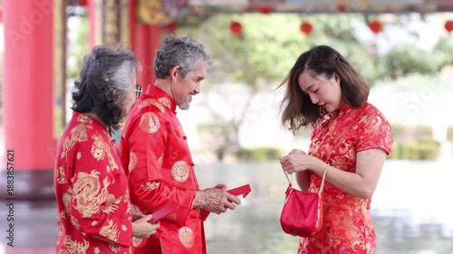 Asian family with senior parent in red cheongsam qipao dress is exchanging fortune tangerine and red envelope at Chinese Buddhist temple during lunar new year for best wish blessing and good luck
