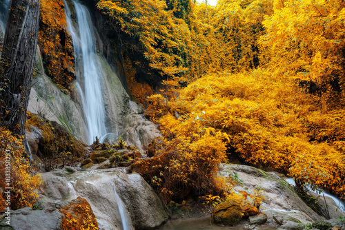 Beautiful waterfall cascading down limestone rocks in a golden autumn forest. Long exposure photography of a scenic stream surrounded by yellow and orange foliage in a tropical park.
