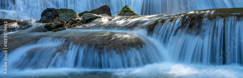 Stunning panoramic close-up of a tiered limestone waterfall with silky water flow. Wide horizontal nature banner background with cascading stream and mossy rocks in a tropical forest.
