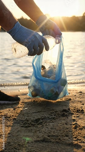 Man in Blue Gloves Collecting Trash in Bag on Sandy Beach at Sunset