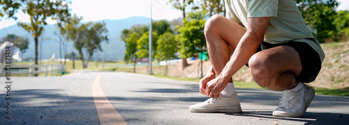 Принти на полотні Young athlete man tying running shoes in the park outdoor, male runner ready for jogging on the road outside, asian Fitness walking and exercise on footpath in morning