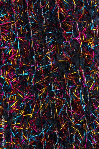 Black fabric interwoven with shiny vibrant strands of blue, gold and red. Great for a background.