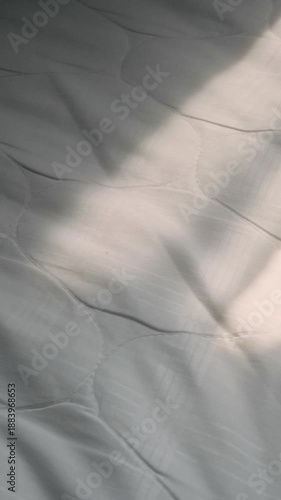 Abstract white bed sheet texture with morning sunlight and shadow, vertical video background, cozy bedroom concept.