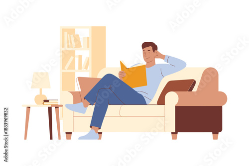 A man relaxing on a couch reading a book and using a laptop