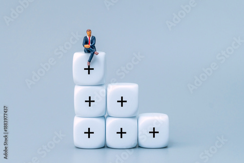 A businessman sitting on a stack of blocks with addition symbols. Value-added employee, progress, human capital, business development concept.