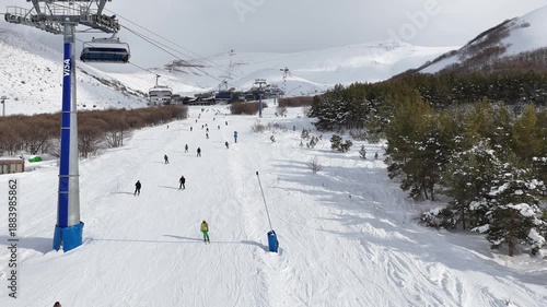 High angle 4K drone footage of a ski resort with ski lifts, and people skiing down a wide mountain slope.