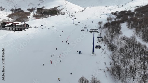High angle 4K drone footage of a ski resort with ski lifts, and people skiing down a wide mountain slope.