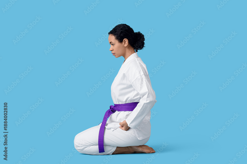 Fototapeta premium Young African-American woman practicing karate on blue background
