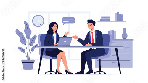 Two business professionals in suits sitting at an office desk and having a discussion while working on a laptop computer.