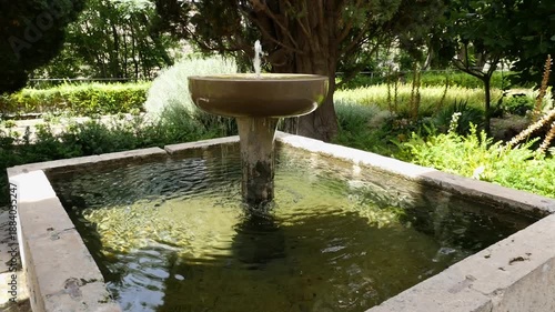 Traditional stone fountain with water flowing into a square pond, surrounded by the lush vegetation of the Nasrid Garden in Vélez de Benaudalla.