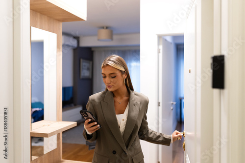 Foto Young blonde woman in a stylish blazer checking her phone while leaving her apartment
