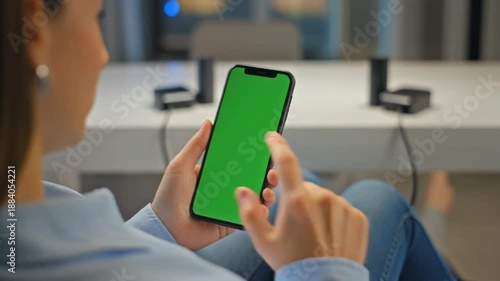 Woman holding green screen smartphone in office setting with white table and charging devices
