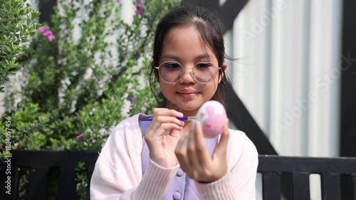 Young asian kid is painting rabbit bunny on easter egg in the outdoor garden for celebrating season festive