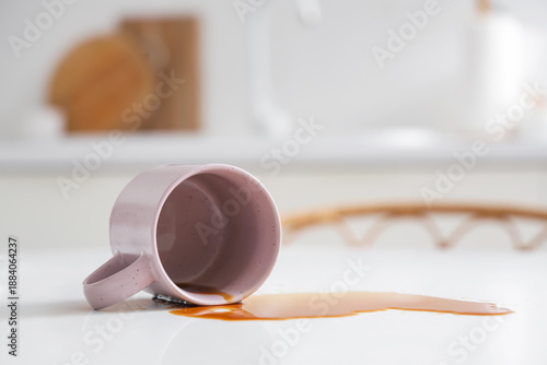 Fotografi Overturned cup and spilled coffee on table in kitchen, closeup