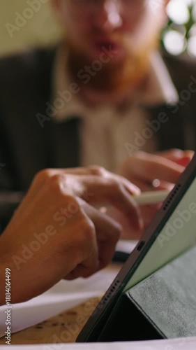 Close-up collaboration with digital tablet as colleagues discuss documents, point at screen, and review important information during focused office meeting