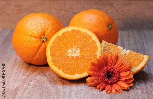 Bright orange whole and sliced oranges with a vibrant gerbera daisy flower create a fresh, juicy, and healthy display on a rustic wooden table, symbolizing natural nutrition and vitality.
