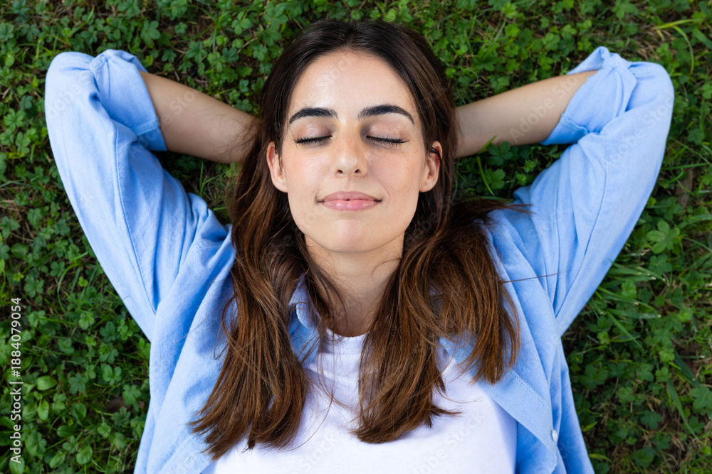 Obraz premium Young woman relaxing on grass with closed eyes