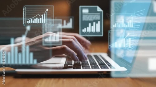 Hands typing on laptop keyboard with floating holographic business charts and financial data documents in professional wooden table setting.