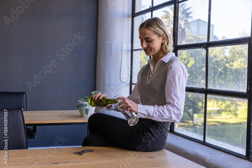 Woman pouring wine from bottle into stemmed glass at studio desk with keys, copy space