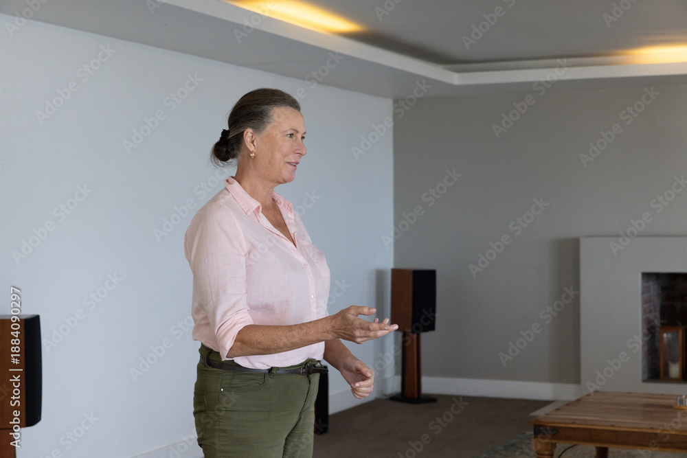 Obraz premium Senior female standing in living room near fireplace, wooden speakers and coffee table, copy space