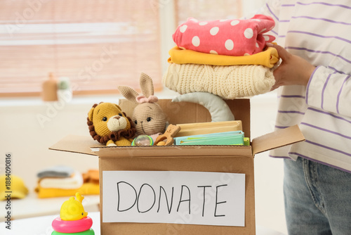 Photography Young woman packing clothes into box with children's toys for donation at home