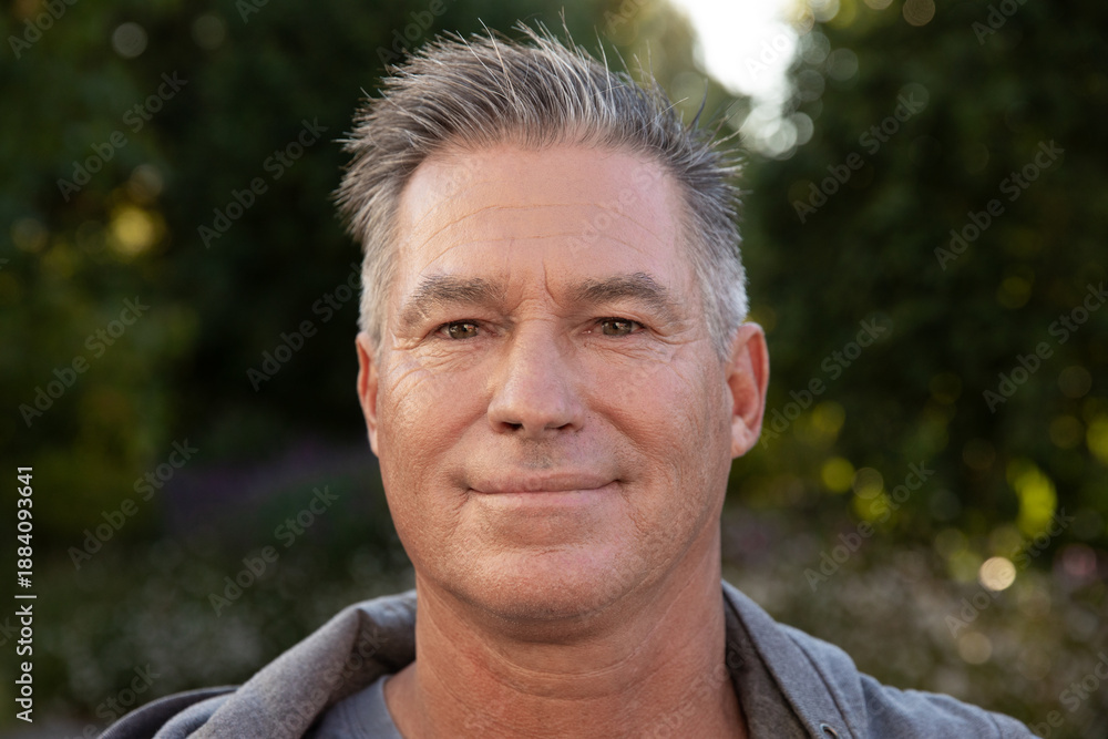 Fototapeta premium Middle-aged man standing calmly in backyard garden wearing hoodie under soft sunlight