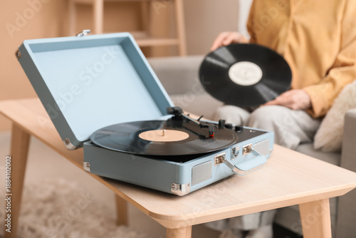 Bild auf Leinwand Young woman with vinyl disk in living room, focus on retro record player