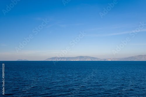 Fotografie A wide expanse of deep blue water stretches toward a distant mountainous coastline under a clear blue sky