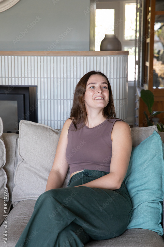 Fototapeta premium Adult female relaxing on beige couch in modern living room by fireplace and potted plant