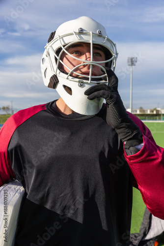 Field hockey goalkeeper adjusting helmet chin strap on turf under floodlights
