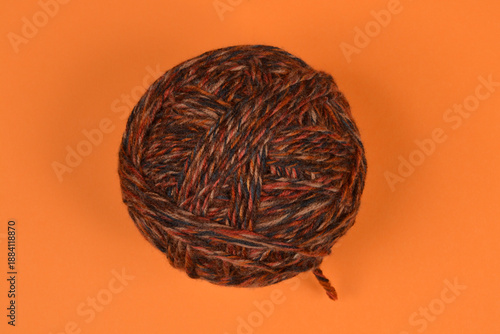 A top view of a large ball of multicolored wool yarn in shades of brown and orange placed on a solid orange surface