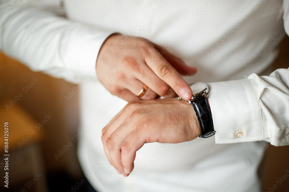 Fototapeta premium A man in a suit is wearing a watch and adjusting his jacket. The image has a blurry quality, which gives it a sense of motion and action. The man's focus on his watch