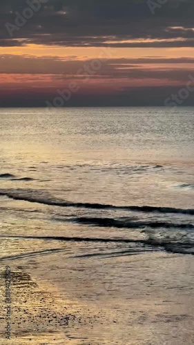 Ocean sunset, Vertical 4K video of a calm scenery of the North Sea water waves slowly moving up and down outdoor at sunset during winter in Noordwijk aan Zee in The Netherlands with space for text.