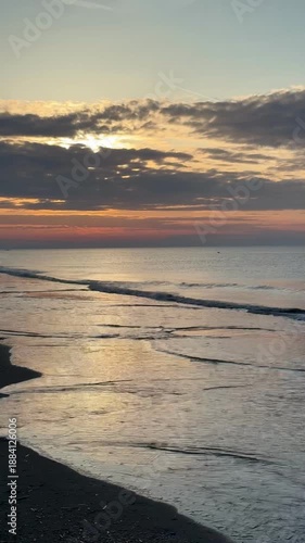 Ocean sunset, Vertical 4K video of a calm scenery of the North Sea water waves slowly moving up and down outdoor at sunset during winter in Noordwijk aan Zee in The Netherlands with space for text.