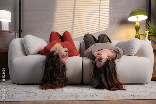 Young women laughing upside down on sofa