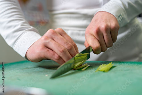 Tableau sur toile Gros plan sur les mains d’un chef coupant un légume sur une planche, avec le couteau en pleine action, illustrant la précision du geste en cuisine professionnelle